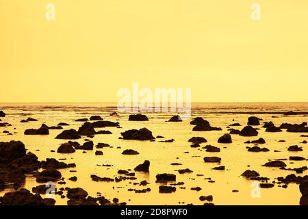 Fantastischer schwarzer Felsstrand in der Abenddämmerung, abstrakte Form von großen Felsen und Steinen, dramatische Sonnenuntergang Himmel Reflexion auf dem Meer. Stockfoto