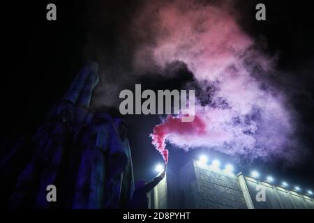 Krakau, Polen. Oktober 2020. Auf einem Denkmal steht während der Demonstration ein Protestler, der ein rosa burendes Fackeln hält.das polnische Verfassungsgericht in seinem neuen, Politisch gewähltes Gerichtsgebäude entschied, dass Abtreibung verfassungswidrig ist in Fällen, in denen es eine hohe Wahrscheinlichkeit von schweren und irreversiblen Schäden am Fötus oder eine unheilbare Krankheit, die sein Leben bedroht. Im Falle Polens bedeutet dies fast ein totales Abtreibungsverbot. Als Folge der Entscheidung des Gerichts begannen große Proteste in jeder größeren Stadt in Polen. Fast eine Woche lang blockierten die Polen den Verkehr auf den Straßen für mehrere Stunden Stockfoto