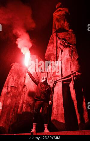 Krakau, Polen. Oktober 2020. Auf einem Denkmal steht während der Demonstration ein Protestler mit einem rot brennenden Fackel.das polnische Verfassungsgericht in seinem neuen, Politisch gewähltes Gerichtsgebäude entschied, dass Abtreibung verfassungswidrig ist in Fällen, in denen es eine hohe Wahrscheinlichkeit von schweren und irreversiblen Schäden am Fötus oder eine unheilbare Krankheit, die sein Leben bedroht. Im Falle Polens bedeutet dies fast ein totales Abtreibungsverbot. Als Folge der Entscheidung des Gerichts begannen große Proteste in jeder größeren Stadt in Polen. Fast eine Woche lang blockierten die Polen den Verkehr auf den Straßen für mehrere Stunden Stockfoto