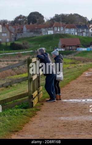 Älteres Paar, das über eine Brücke auf einem Fußweg bei Brunnen am Meer oder blakeney an der nördlichen norfolkküste geht Stockfoto