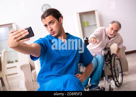 Alter Mann im Rollstuhl und schlechter Betreuer drinnen Stockfoto