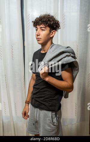 Attraktiver junger Mann mit lockigen Haaren trägt schwarzes T-Shirt posiert auf weißen Vorhängen Hintergrund. Modekonzept Stockfoto