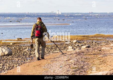 Ein Schatzsucher mit einem Metalldetektor geht am menschenleeren Sandstrand entlang auf der Suche nach verlorenen Münzen und Schmuck. Stockfoto