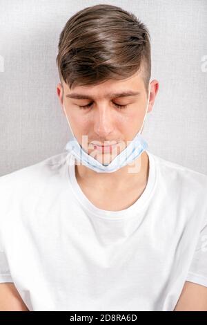 Müde junger Mann in einer Grippe-Maske an der Wand Im Zimmer Stockfoto