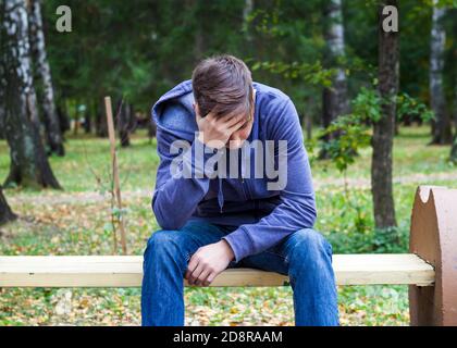 Trauriger junger Mann sitzt auf der Bank im Herbstpark Stockfoto