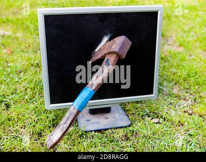 AX zum Zertrümmern eines Computerbildschirms auf dem Grashintergrund Stockfoto