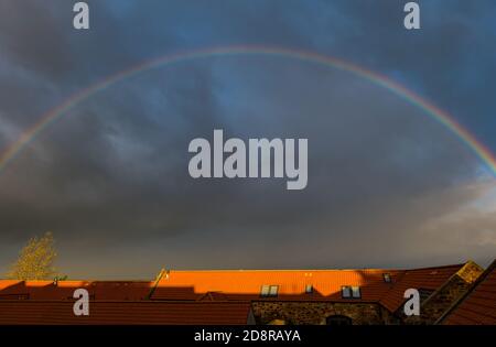 East Lothian, Schottland, Großbritannien, 1. November 2020. UK Wetter: Ein Regenbogenbogen beleuchtet den Himmel über Hausdächern an einem stürmischen Duschtag mit einem sehr dunklen stürmischen Himmel Stockfoto