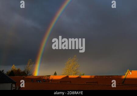 East Lothian, Schottland, Großbritannien, 1. November 2020. UK Wetter: Ein doppelter Regenbogen beleuchtet den Himmel über Hausdächern an einem stürmischen Duschtag mit einem sehr dunklen stürmischen Himmel Stockfoto