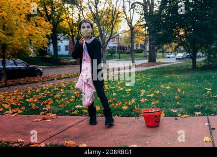 Eine junge Trick-or-treater legt während Oakwoods erstem 'COVID-19 Halloween' Süßigkeiten in ihre Tasche und trägt eine Schutzmaske. Normalerweise erwartet Volusia Hunderte von Trick-or-Treatern, aber während des ersten "COVID-19 Halloween" in Amerika spielten Eltern es sicher, Familien trugen Masken mit ihren Kostümen und Eltern sorgten dafür, dass ihre Kinder ihre Masken nicht auszogen oder zu nahe an diejenigen kamen, die sie nicht kannten, aufgrund von Coronavirus-Ängsten. Viele entschieden sich ganz aus den Festlichkeiten, aber diejenigen, die aus wagten, wurden mit Eimern voller Süßigkeiten und gutherzige, aber distanzierte Wellen von Nachbarn erfüllt. Stockfoto