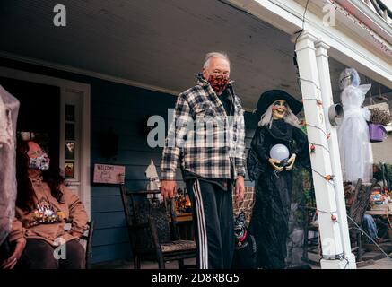 Zwei Hausbesitzer sitzen auf ihrer festlichen, geschmückten Veranda, während sie warten, um Süßigkeiten an Trick-or-treaters während Oakwoods erstem "COVID-19 Halloween" zu übergeben. Normalerweise erwartet Volusia Hunderte von Trick-or-Treatern, aber während des ersten "COVID-19 Halloween" in Amerika spielten Eltern es sicher, Familien trugen Masken mit ihren Kostümen und Eltern sorgten dafür, dass ihre Kinder ihre Masken nicht auszogen oder zu nahe an diejenigen kamen, die sie nicht kannten, aufgrund von Coronavirus-Ängsten. Viele entschieden sich ganz aus den Festlichkeiten, aber diejenigen, die aus wagten, wurden mit Eimern voller Süßigkeiten und gutherzig, aber DIS erfüllt Stockfoto