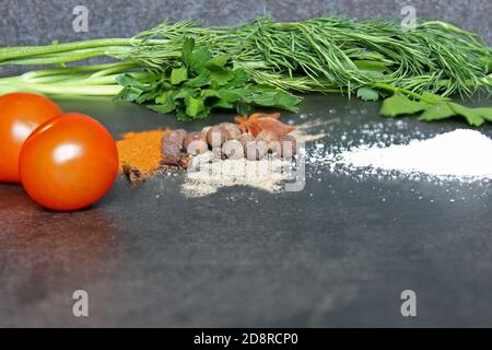 Verschiedene Arten von Gewürzen, Dill, Petersilie, Kirschtomaten auf schwarzem Stein Hintergrund. Café-Konzept. Köstliche Lieferung Stockfoto
