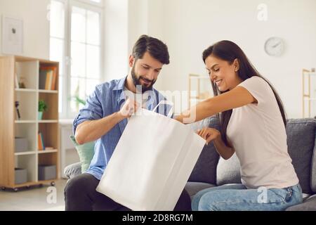 Glücklich junges Paar sitzt auf der Couch mit Papiertüte und Auspacken von frischen Lebensmitteln zum Mitnehmen Stockfoto