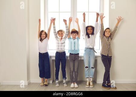 Eine Gruppe verschiedener Kinder von Klassenkameraden stehen mit erhobenen Händen im Schulkorridor. Stockfoto