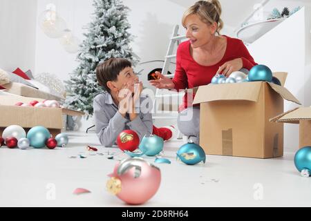 Frohe Weihnachten und schöne Feiertage! Mutter und Sohn schmücken den Weihnachtsbaum im Haus. Versehentlich bricht das Kind die Bälle, die Mutter schimpft h Stockfoto