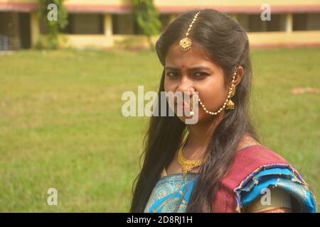 Nahaufnahme eines indischen bengalischen Teenager-Mädchen mit langen dunklen Haaren tragen traditionelle Sari und Schmuck Nasenring, Ohrring, Halskette und Maang tika Stockfoto