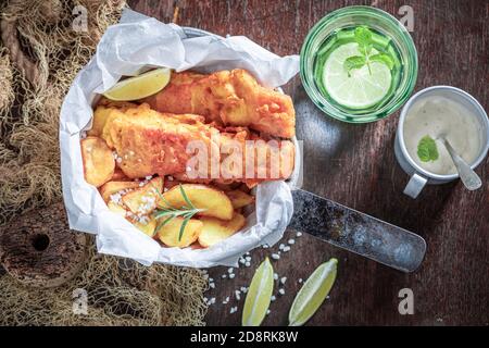 Hausgemachter Fisch und Pommes mit Saucen und Limette serviert Holztisch Stockfoto