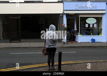 Ayr, Ayrshire, Schottland, Vereinigtes Königreich . Ehrliche Straßenfotografie rund um Ayr. Eine Frau mit Kapuze schaut sich das Café zum Mitnehmen in einer leeren Straße an Stockfoto