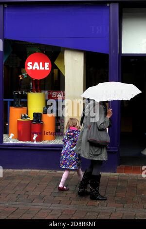 Ayr, Ayrshire, Schottland, Vereinigtes Königreich . Ehrliche Straßenfotografie rund um Ayr. Frau mit Kind geht an einem Schuhgeschäft mit Verkaufsnotice vorbei Stockfoto