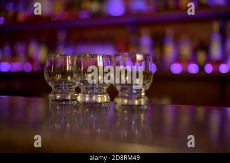 Drei kleine Glas Tassen, an der Bar im Licht der lila Lichter Schaufenster. Stockfoto