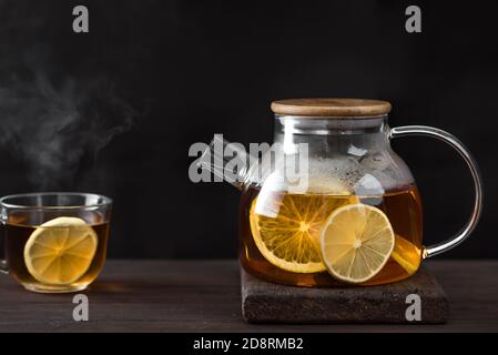 Zitrustee mit Zitrone, Orangen in durchsichtiger Glas Teekanne auf dunklem Holztisch, Kopierraum. Früchtetee. Saisonaler Winter Herbst heißer Drink. Stockfoto