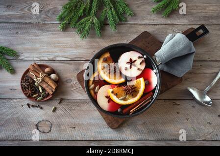 Weihnachtlicher Glühwein mit Gewürzen, Äpfeln und Orangen auf rustikalem Holztisch. Traditionelles Heißgetränk für Weihnachten und Winterferien. Stockfoto