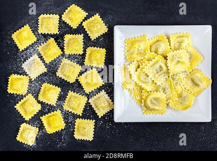 Ravioli mit Mehl und Basilikum auf schwarzem Hintergrund. Italienische Ravioli Herstellung Prozess. Draufsicht Stockfoto