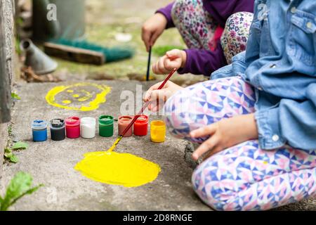 Kleine Kinder malen auf Beton, zwei anonyme Mädchen, die sich an Kunsttherapie-Aktivitäten beteiligen. Kleine Kinder verbreiten bunte Farbe auf dem Boden Stockfoto