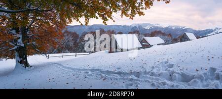 Herbstlandschaft mit dem ersten unerwarteten Schnee. Alte hölzerne Schäferhütten auf einem Berg. Verschneite Strecke Stockfoto