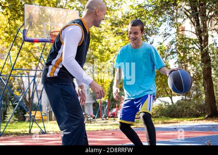 Brüder spielen Basketball eins auf eins. Älterer Bruder, der seinem jüngeren Bruder die besten Züge im Spiel beibringt. Sport und gesunder Lebensstil. Stockfoto