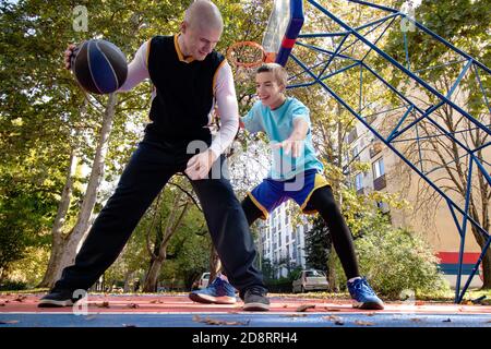 Brüder spielen Basketball eins auf eins. Älterer Bruder, der seinem jüngeren Bruder die besten Züge im Spiel beibringt. Sport und gesunder Lebensstil. Stockfoto