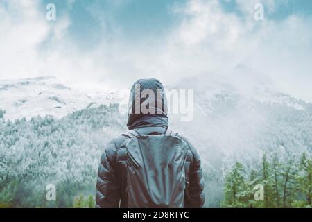 Rückansicht einer Person, die vor einer leicht schneebedeckten Bergkette steht. Stockfoto
