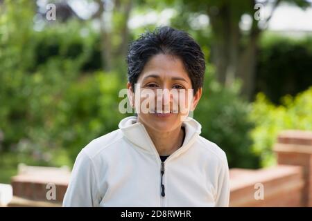 Casual Portrait einer indischen Frau lächelnd. British Asian (BAME) steht im Freien in einem Garten, Großbritannien Stockfoto