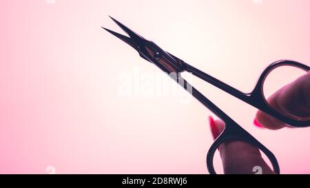 Maniküre Nagelhaut Schere in den Fingern der Frauen in rosa Licht. Stockfoto