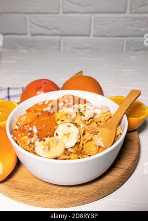 Maisflocken Schüssel mit Milch, Persimmon, Orange auf Holzbrett auf weißem Hintergrund, gesundes Frühstück Stockfoto
