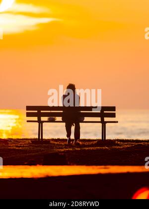 Einsame junge Frau sitzt auf Holzbank und beobachtet den Sonnenuntergang in Basanija in der Nähe von Savudrija, Istrien Küste in Kroatien Europa Stockfoto