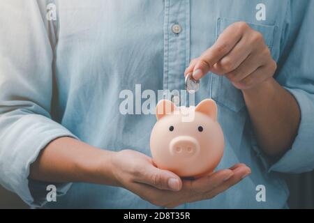 Weibliche Hände legt eine Münze in ein rosa Sparschwein. Das Konzept des Sparens. Stockfoto