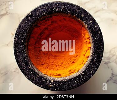 Lebhaftes Orange aus Kurkuma Gewürz in dunklem Steinmörtel und Stößel Stockfoto