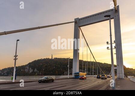 Autos fahren über die Erzsebet / Elisabeth Brücke in Budapest Zur goldenen Stunde mit dem Gellertberg im Hintergrund Stockfoto