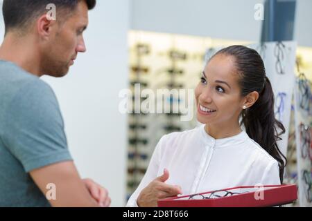 Arbeiterin, die dem Mann im Optikgeschäft eine Brille anbietet Stockfoto