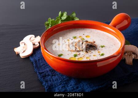 Lebensmittelkonzept Bio Pilz Sahne Suppe in orange Keramik Griff Schale auf schwarzem Schieferstein mit Kopierraum Stockfoto