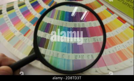 Überprüfung des Vergrößerungsglases auf der Farbpalette. Auswählen von Farben aus Katalogproben zum Drucken von Proofs. Konzept des Farbmanagements im Druck Stockfoto