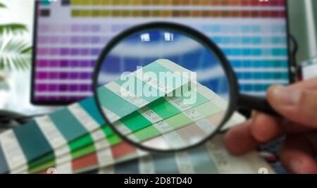Überprüfung des Vergrößerungsglases auf der Farbpalette. Auswählen von Farben aus Katalogproben zum Drucken von Proofs. Konzept des Farbmanagements im Druck Stockfoto