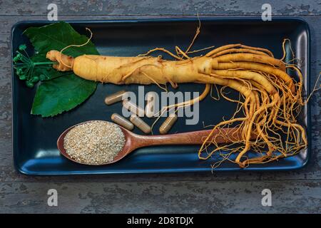 Frische Ginseng Wurzel auf schwarzem Teller mit Pulver für Kapseln Medizin Stockfoto