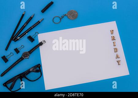 Briefpapier und leeres Blatt auf blauem Hintergrund. Die Inschrift Freitag auf einem Blatt von Holzbuchstaben. Stockfoto