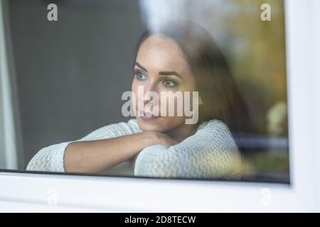 Deprimierte Frau schaut hinter dem Fenster mit einem traurigen Gesichtsausdruck hervor. Stockfoto