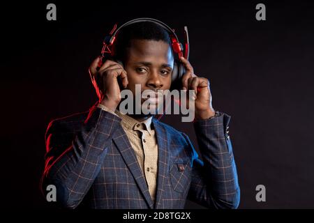 afroamerikanischer Mann, der in dunklen Kopfhörern Musik hört. Portrait von stilvollen DJ mit Headset, trägt Karomuster, isoliert auf schwarzem Hintergrund Stockfoto