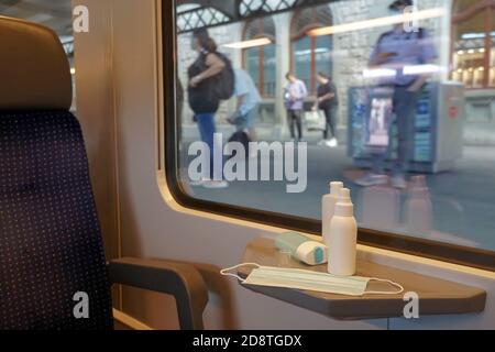 Neue normale pendeln und Reisen mit Gesichtsmasken und Handdesinfektionsmittel im Zugwagen angezeigt. Der Zug ist am Bahnhof. Stockfoto