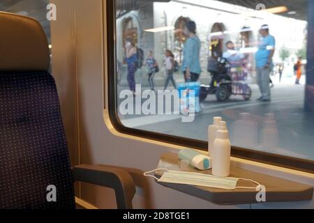 Neues normales Pendeln mit Gesichtsmasken und Handdesinfektionsmitteln, die im Zugwagen angezeigt werden. Der Zug ist am Bahnhof und die Passagiere tragen Gesichtsmasken. Stockfoto