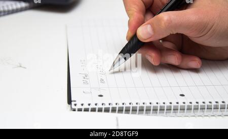 Der Student löst mathematische Formeln. Der Mensch schreibt mit einem Stift in ein Notizbuch. Hausaufgaben. Notizen in einem Notizbuch. Stockfoto