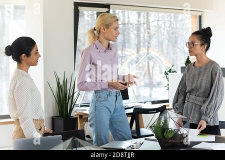 Fokussierte blonde junge Geschäftsfrau diskutieren Arbeitsfragen mit multirassischen Kollegen. Stockfoto